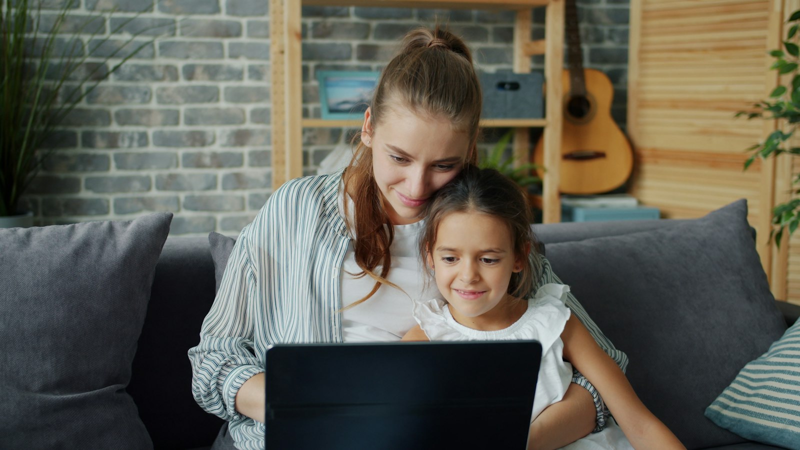 Une maman et sa fille souriantes devant un ordinateur, sur un canapé